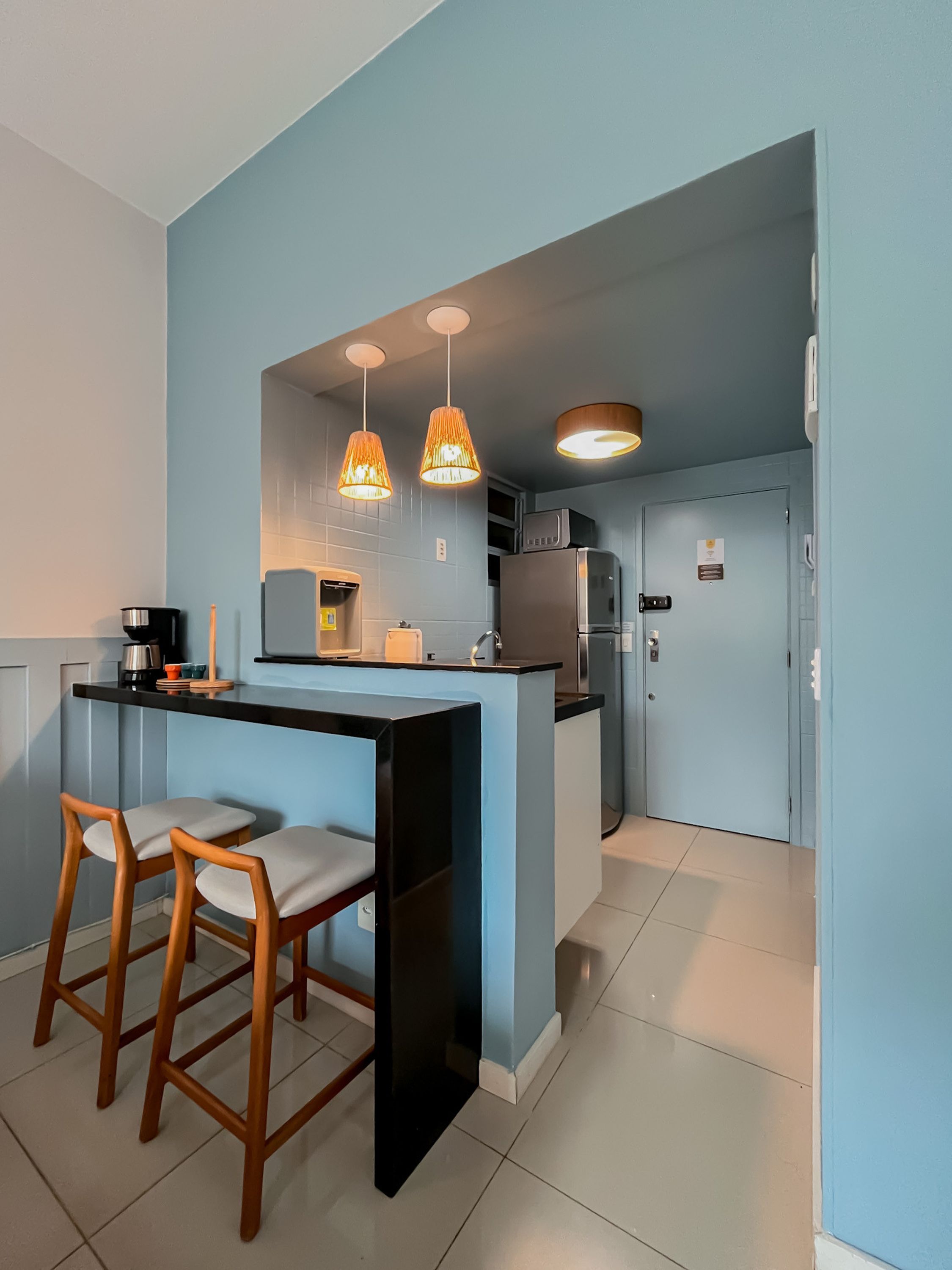 Cocina moderna con una isla central, taburetes de bar, iluminación colgante y un refrigerador.