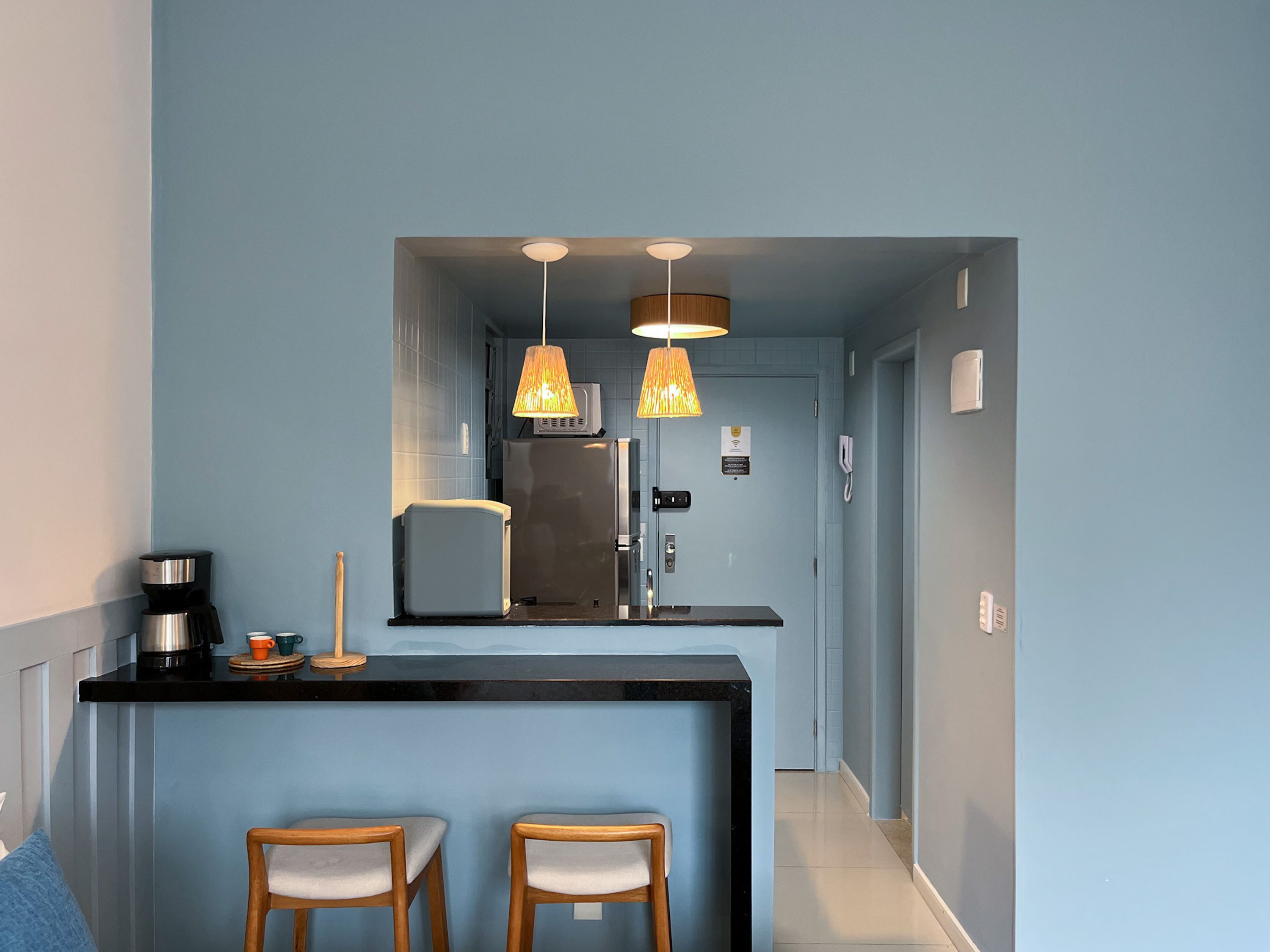 Een keuken met een zwart aanrecht, twee houten barkrukken, een koffiezetapparaat en hanglampen.