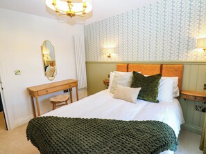 Ein Schlafzimmer mit einem Bett, einem Nachttisch, einer Kommode, einem Spiegel und einer Wandleuchte.