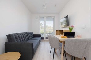 Un soggiorno moderno con un divano, un tavolo da pranzo con sedie, una TV a parete e una finestra vista all'esterno.