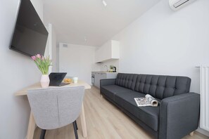 Ein modernes Wohnzimmer mit einem grauen Sofa, einem Holzesstisch mit einem Laptop und einer Blumenvase, und einer Küche im Hintergrund.