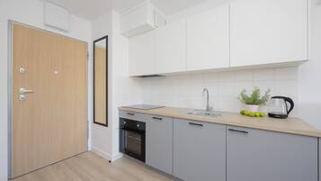 A modern kitchen with a wooden door, white cabinets, a sink, and a kettle on the counter.