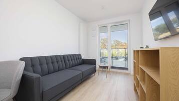 Un salon moderne avec un canapé gris, une bibliothèque en bois et un téléviseur fixé au mur.
