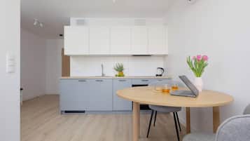 A modern kitchen with white cabinets, a wooden countertop, and a sink. There is a round table with a laptop, a glass of tea, and a loaf of bread.