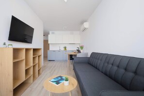 Un espace de vie moderne comprenant un canapé, une table basse, un téléviseur à écran plat et un coin cuisine.