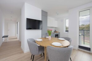Un comedor moderno con una mesa redonda, sillas grises, un televisor de pantalla plana montado en la pared y vistas al exterior a través de un ventanal grande.