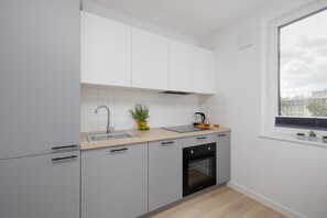 Une cuisine moderne équipée d’un four encastré, d’un évier et d’une fenêtre donnant sur des immeubles.