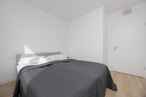A minimalist bedroom with a bed, a door, and a light switch on the wall. - Warsaw | Grenadierów 41 | Comfortable Apartment | Air Conditioning (Warszawa)