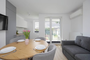 A modern kitchen with white cabinets, a dining table with plates and cutlery, and a grey sofa. - Warsaw | Grenadierów 41 | Comfortable Apartment | Air Conditioning (Warszawa)