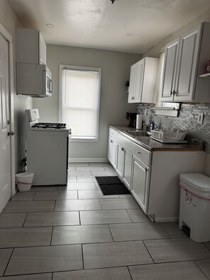 A kitchen with white cabinets, a built-in microwave, a stove, and a window with blinds. - Tranquil 2-bedroom apartment with AC in vibrant Detroit (Detroit)