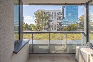 A balcony with a glass railing overlooking a grassy area and modern buildings. - Warszawa | Grenadierów 41 | Air Conditioned Studio | Desk (Warszawa)