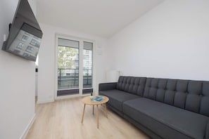 Una sala moderna con un sofá gris, una mesita redonda de madera y un ventanal corredizo que da a un balcón.