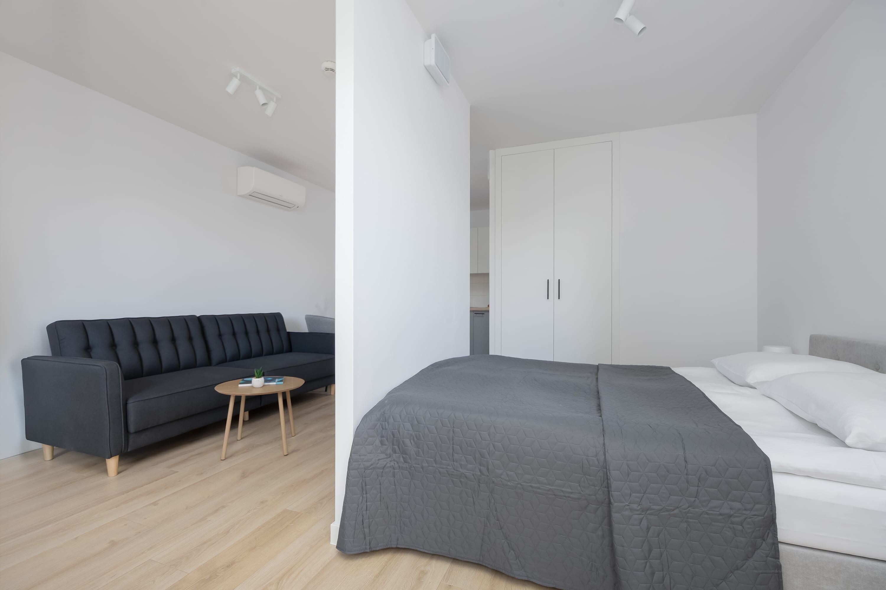 Un dormitorio moderno con cama, un sofá gris oscuro, una mesita redonda y un armario.