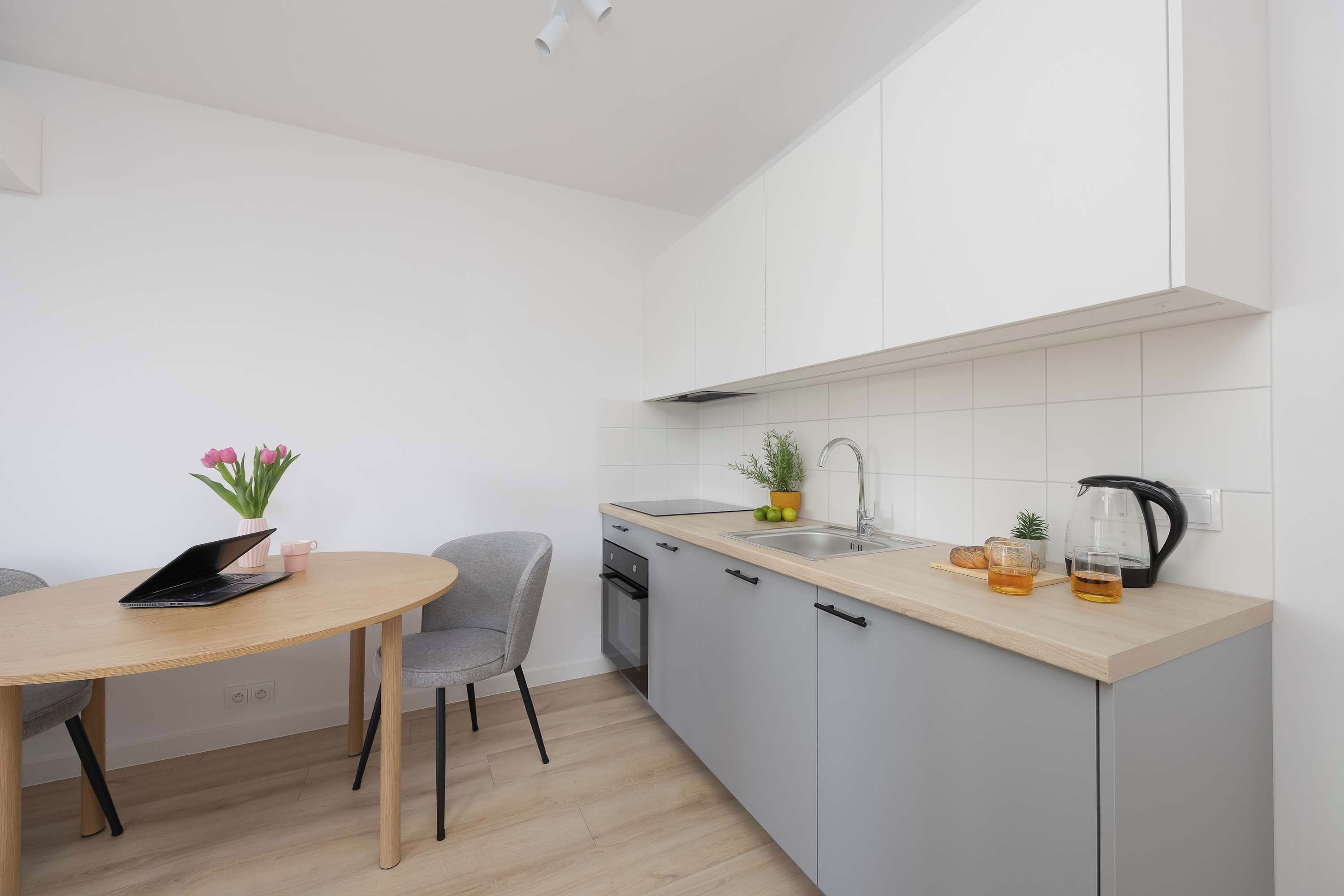Una cocina moderna con zona de comedor, que incluye un ordenador portátil sobre la mesa, un fregadero y un hervidor.