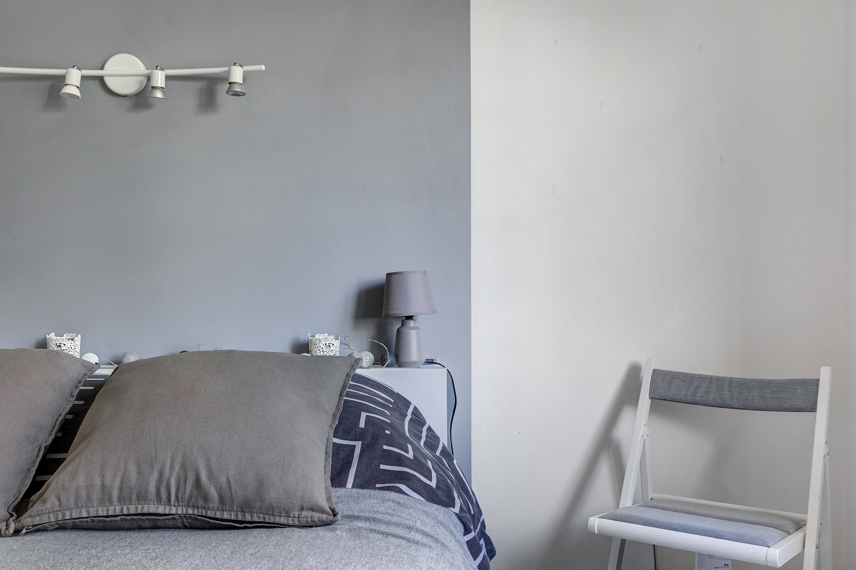 A bedroom with a bed, pillows, a bedside table with a lamp, and a chair.