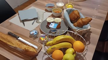 A dining table with food items, a bread roll, a fruit basket, and a vase with flowers.