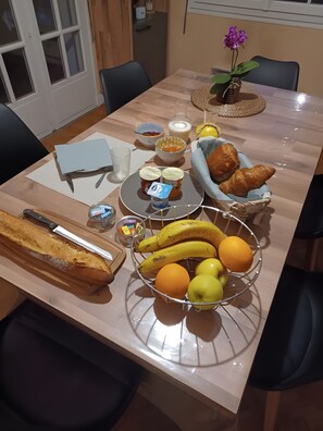 A dining table with food items, a bread roll, a fruit basket, and a vase with flowers. - Guest Room 'Laurentine' with Shared Terrace, Shared Garden and Wi-Fi (Montval-sur-Loir)