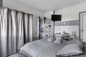 A modern bedroom with a bed, a TV, a desk, and a shelf with various items.