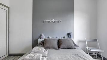 Een slaapkamer met een bed, kussens, een nachtkastje met een lamp en een stoel.