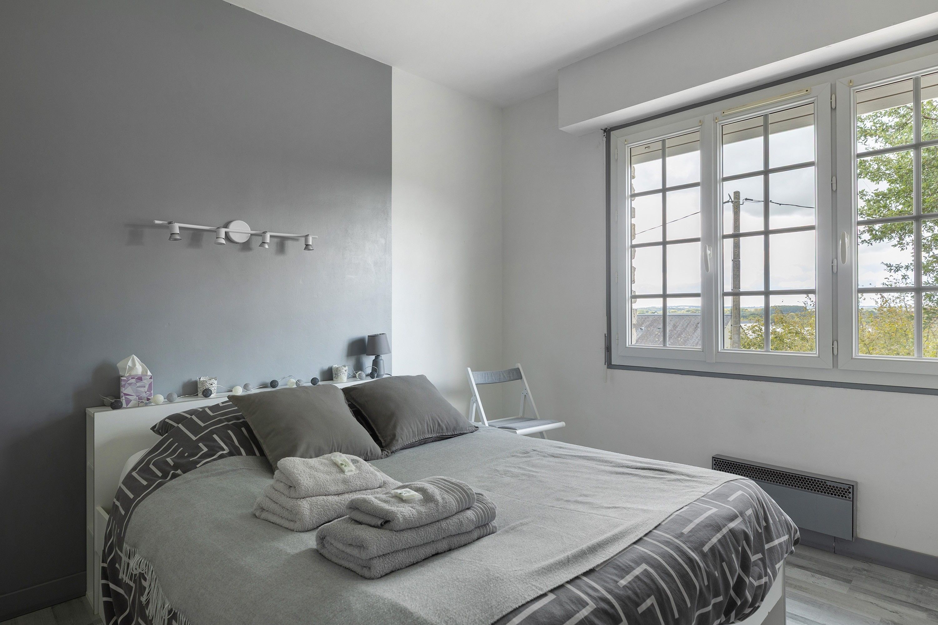 Une chambre moderne avec un grand lit, une table de chevet avec une lampe et une fenêtre donnant sur un beau paysage.