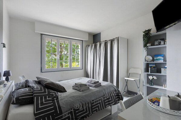 A modern bedroom with a bed, a desk, a chair, a TV, and a window with curtains.