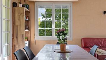 Un coin repas comprenant une table, des chaises, une plante en pot et une fenêtre donnant sur des arbres.