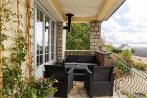 A balcony with wicker furniture, a stone wall, and a view of the surrounding area.