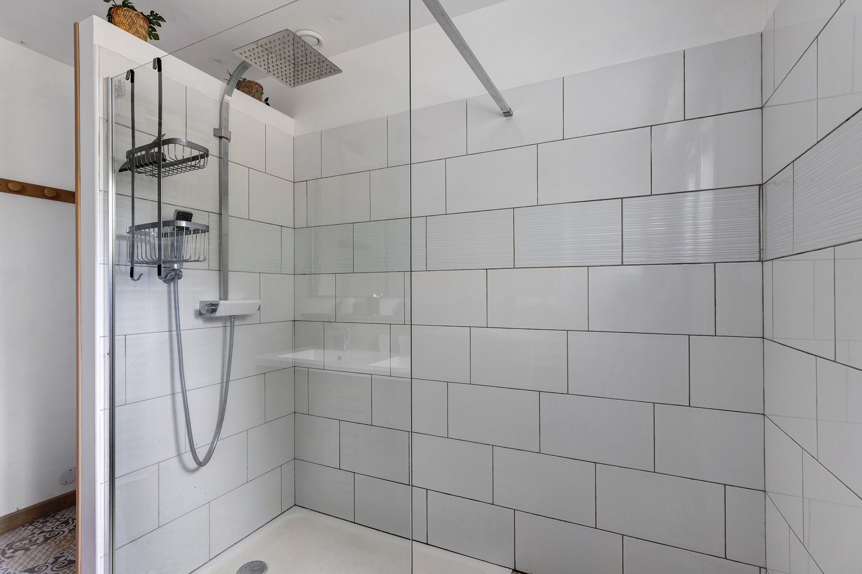 Un espace douche moderne doté d’une porte en verre, d’un pommeau de douche à main et d’un pommeau de douche à pluie fixé au mur.