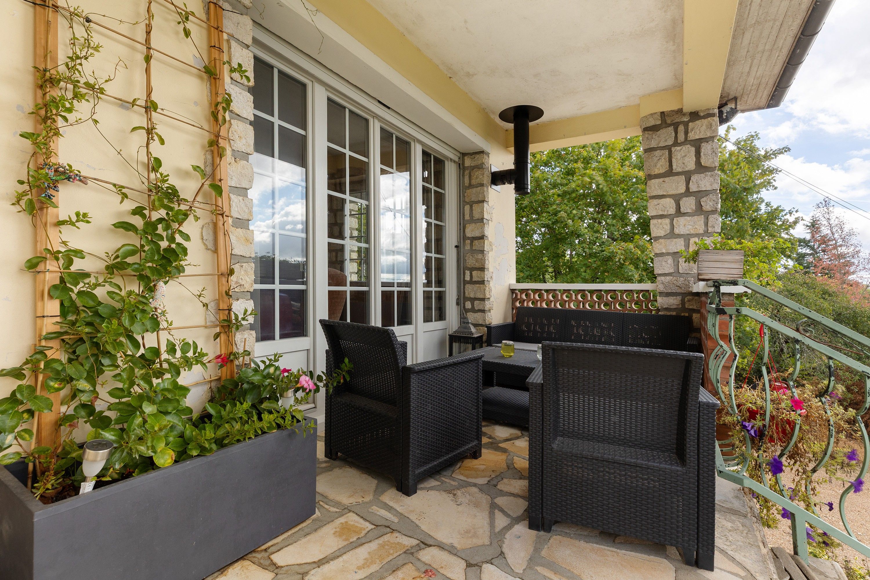 A covered outdoor seating area with wicker furniture and potted plants.