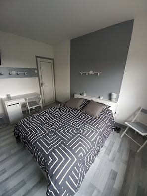 Een slaapkamer met een bed, een bureau, een stoel en een nachtkastje.