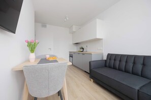 A modern living room with a grey sofa and a dining area with a table and chairs. - Warsaw | Grenadierów 41 | Elegant Apartment | Air Conditioning (Warszawa)