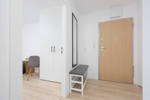 Ein Zimmer mit einem weißen Kleiderschrank, einem Schreibtisch mit Stuhl, einer Holztür und einer Bank.