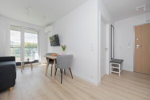 A modern living room with a sofa, a dining table with chairs, a flat-screen TV mounted on the wall, and a sliding door leading to another room. - Warsaw | Grenadierów 41 | Elegant Apartment | Air Conditioning (Warszawa)