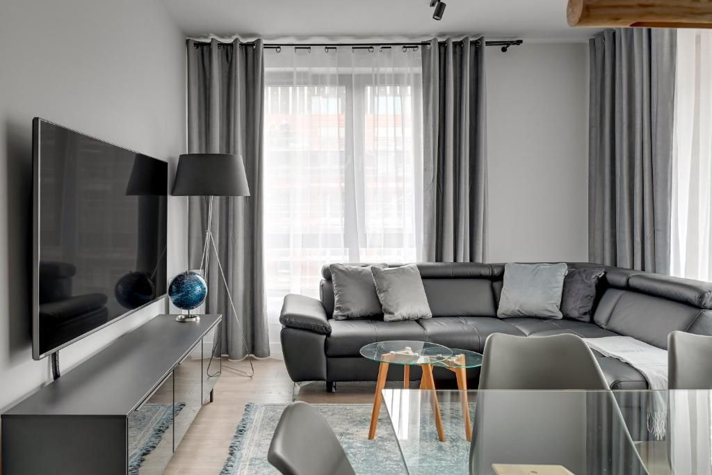A modern living room with a flat-screen TV, a leather sofa, a glass coffee table, and a lamp.