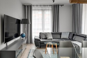A modern living room with a flat-screen TV, a leather sofa, a glass coffee table, and a lamp. - Premium Apartment Mustang with Parking (Gdańsk)