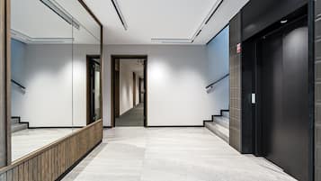 A modern hallway with a marble floor, a wooden railing, and a black elevator door.