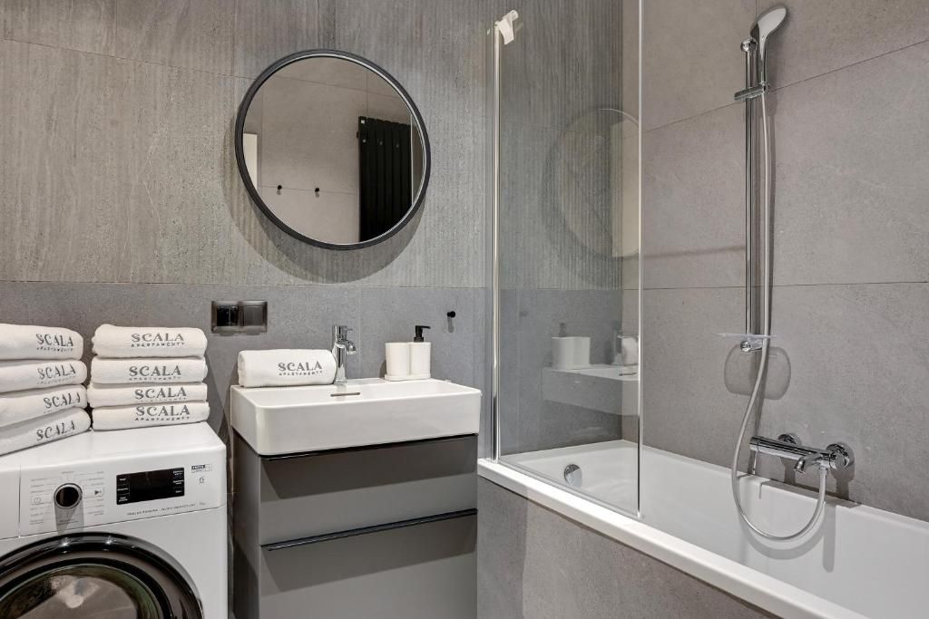 A modern bathroom with a round mirror, a white sink, a glass-enclosed shower, and a stack of towels.