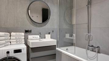 A modern bathroom with a round mirror, a white sink, a glass-enclosed shower, and a stack of towels.