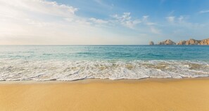 A beach with clear water and distant rocky formations. - 2 bedroom suite with breathtaking oceanfront view! (Cabo San Lucas)