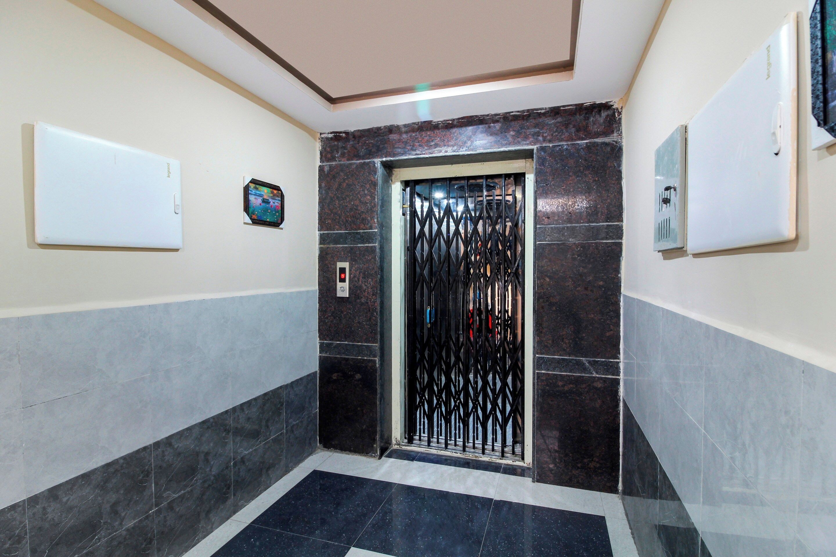 Un pasillo con piso de baldosas, una puerta con reja metálica y un panel de control de ascensor fijado a la pared.