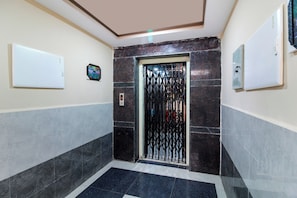 A hallway with a tiled floor, a door with a metal security gate, and a wall-mounted elevator control panel. - Super Hotel O New Cyber Grand Madhapur (Hyderabad)