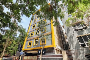 A multi-story building with a distinct yellow and grey facade, a visible entrance with a metal gate, and a tree in the foreground. - Super Hotel O New Cyber Grand Madhapur (Hyderabad)