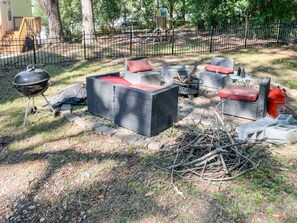 Un área de estar al aire libre con una parrilla, sillas y un pozo de fuego.