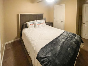Una habitación de hotel con una cama, dos almohadas, una mesita de noche y una puerta.