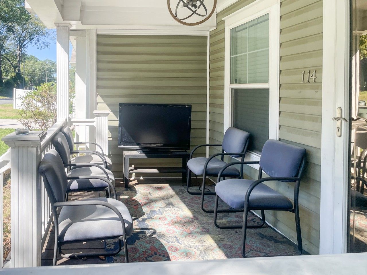 Eine überdachte Veranda mit einem Flachbildfernseher, sechs Stühlen und einem gemusterten Teppich.