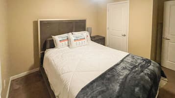 Un dormitorio con cama, almohadas, mesita de noche y puerta.
