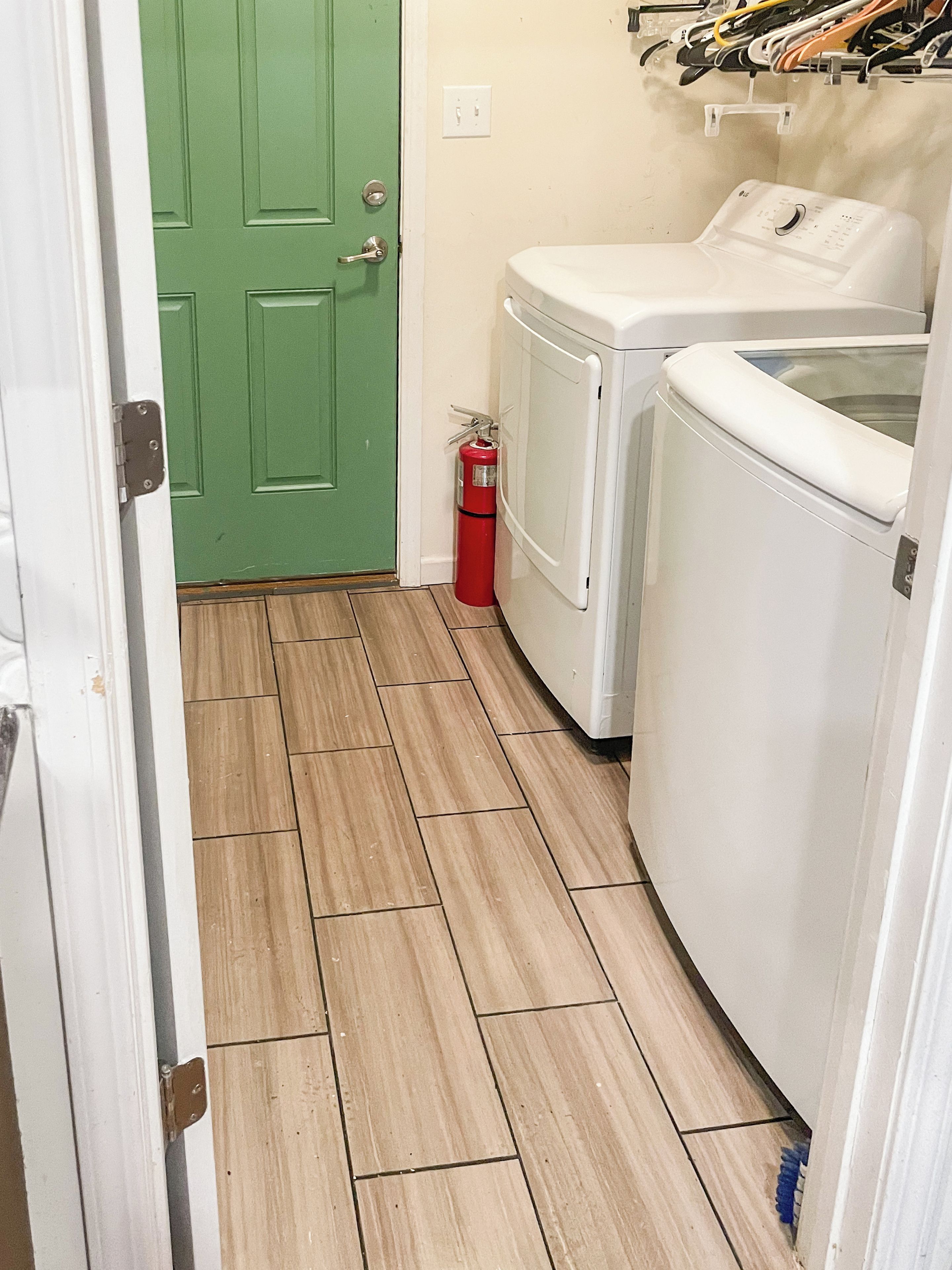 A laundry room with a green door, a white washing machine, and a red fire extinguisher.