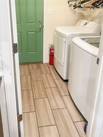 Un cuarto de lavandería con una puerta verde, una lavadora blanca y un extintor de incendios rojo.