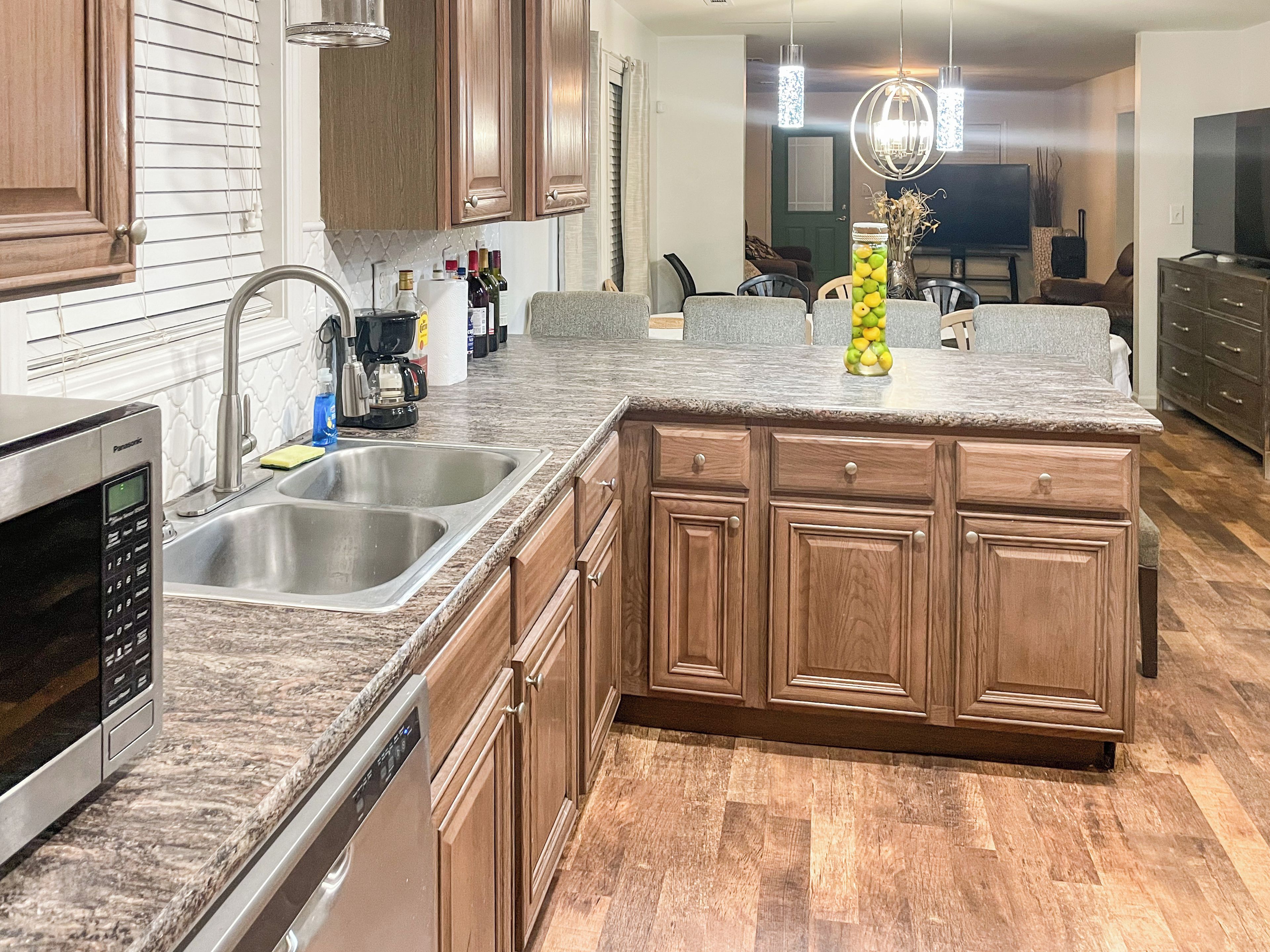 A kitchen with wooden cabinets, a granite countertop, stainless steel appliances, and a dining area with a chandelier.