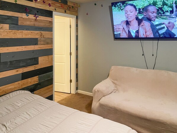Une chambre à coucher avec un lit, un téléviseur fixé au mur et un mur recouvert de panneaux en bois.
